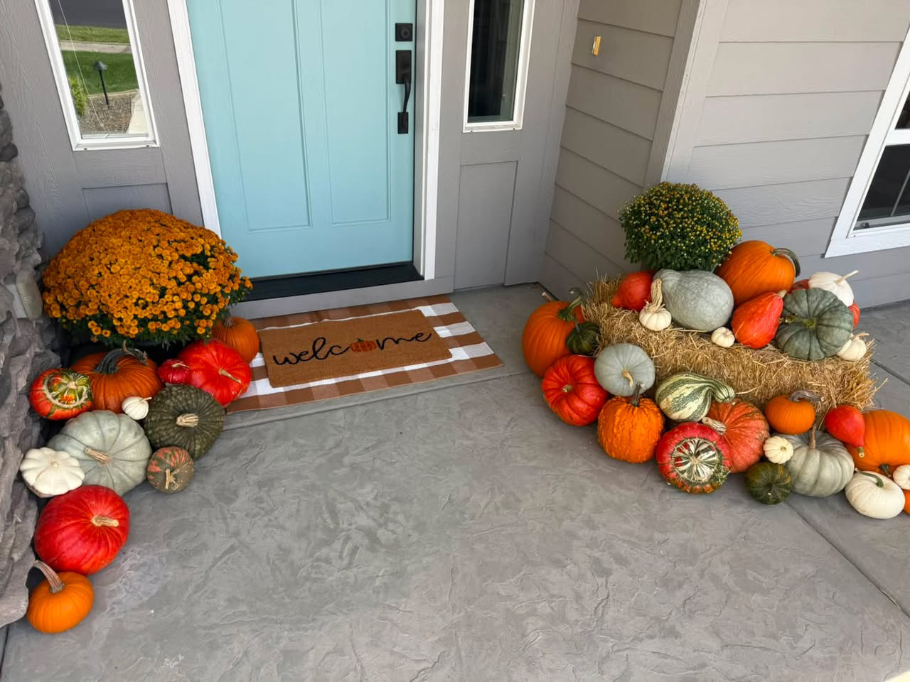 Porch styled with a wagon, hay bales, pumpkins, and a harvest sign